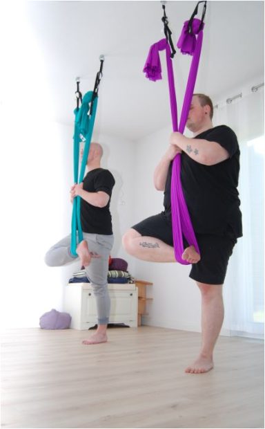 Männer Yoga Zwei Personen üben mit Tuch im Gleichgewicht, eine in türkis, die andere in lila.